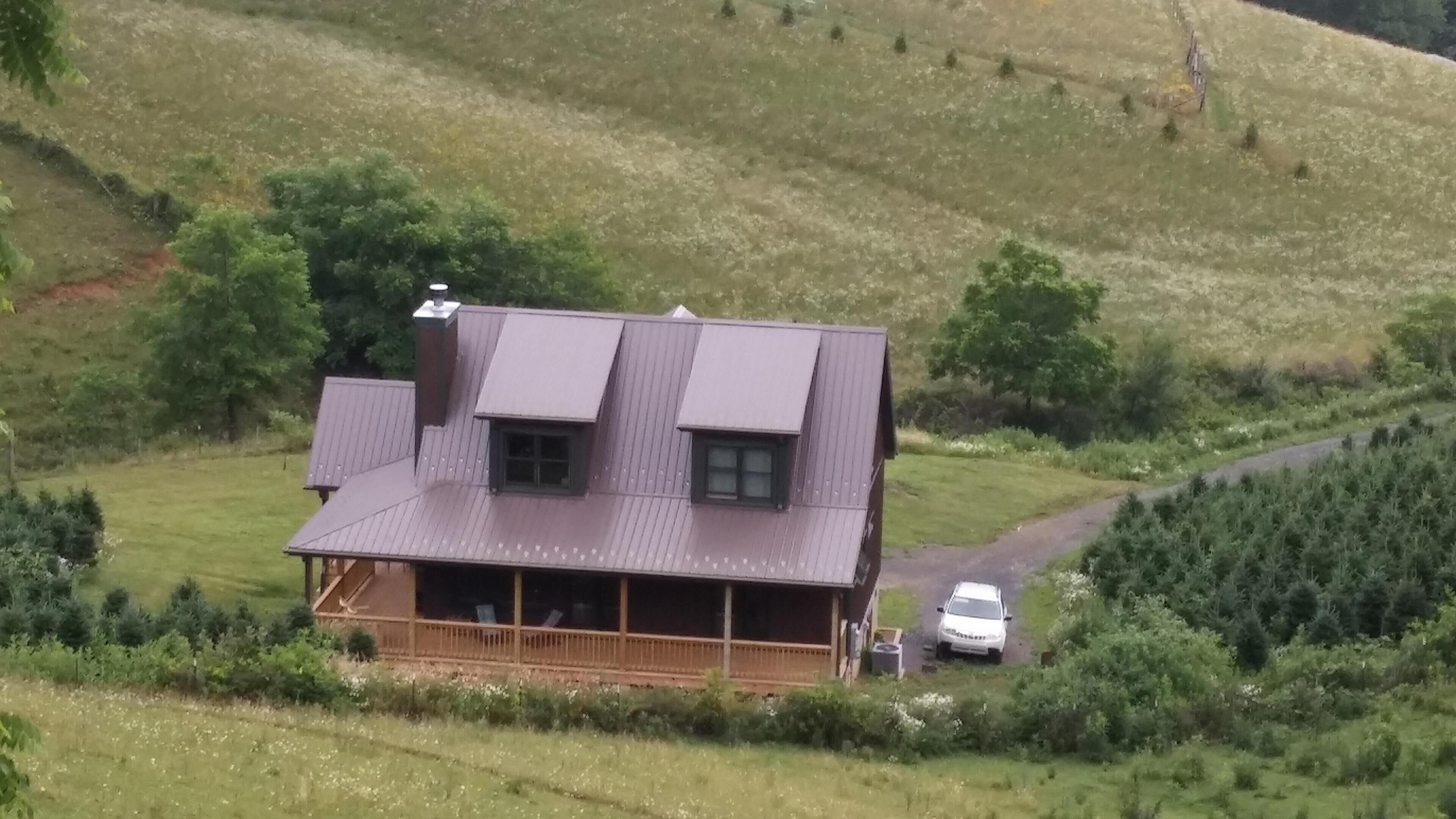 A two-story house with a sloped roof, a porch, and a driveway leading to a parked car.