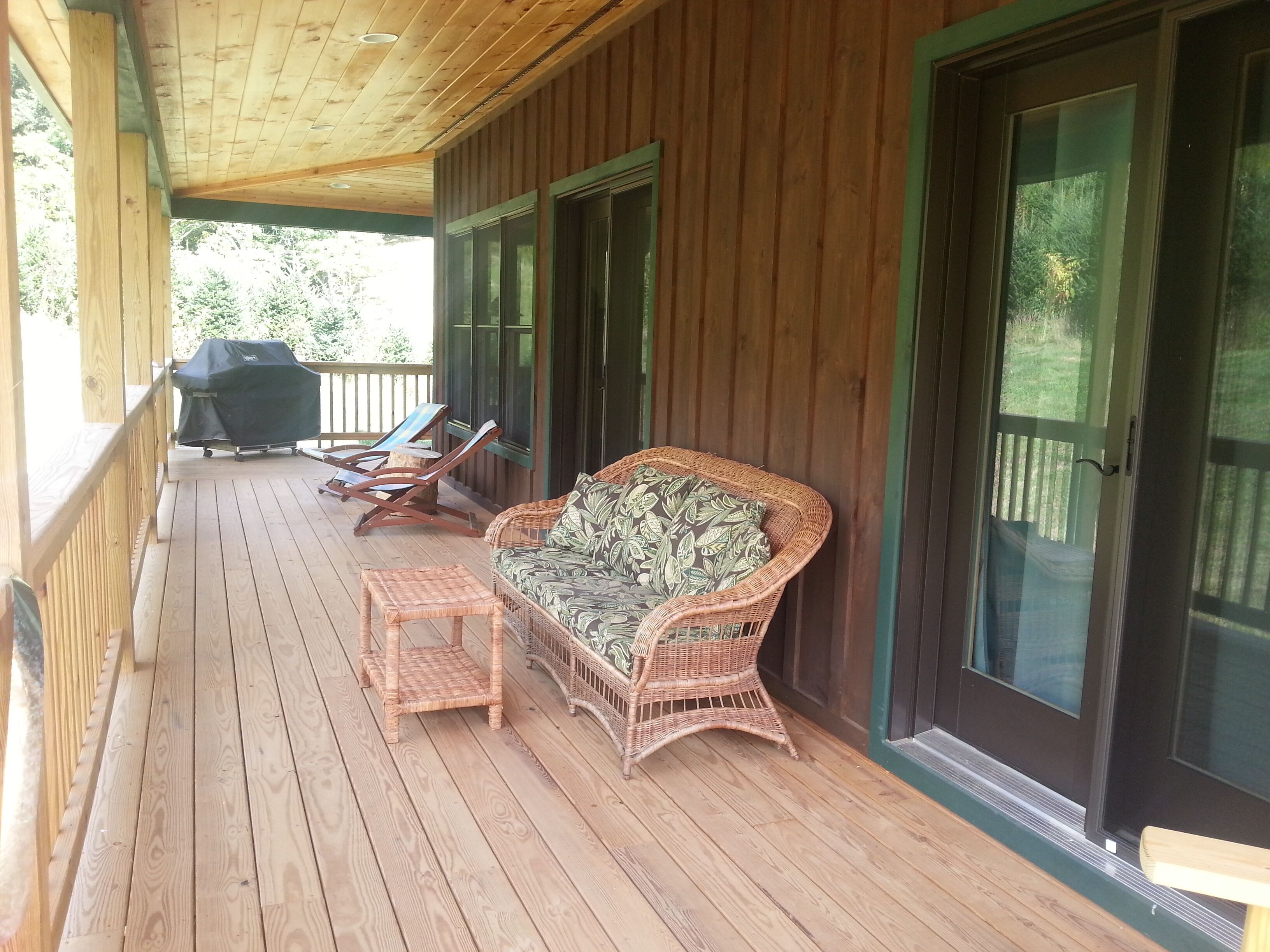 A covered porch with wicker furniture, a grill, and a sliding glass door.