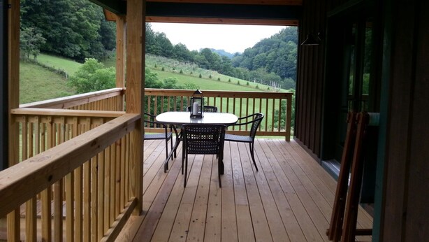 A wooden deck with a table and chairs, overlooking a green landscape.