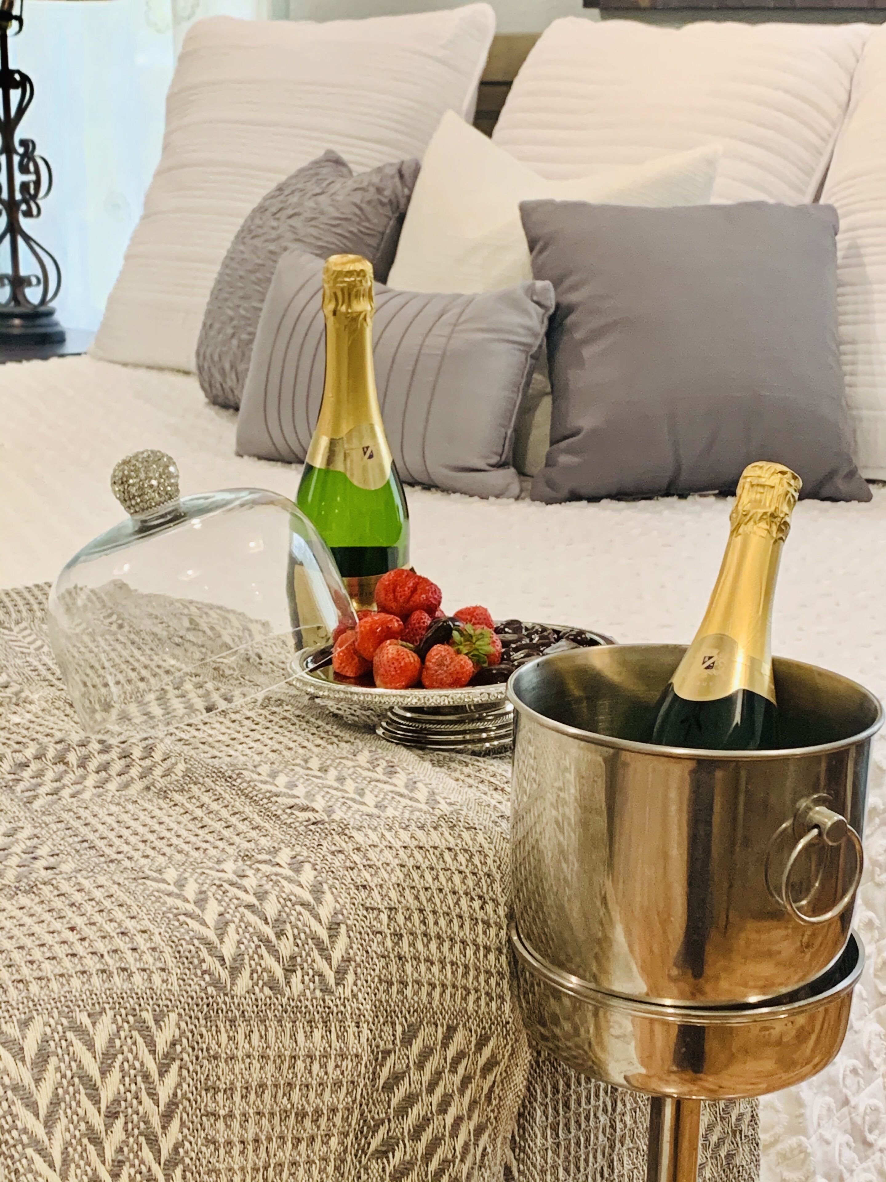 Ein Bett mit einer Glaskuppel, zwei Champagnerflaschen, einer Schale mit Erdbeeren und einer gewebten Decke.