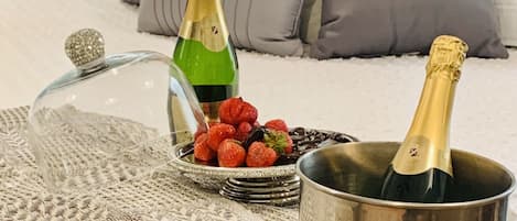 Ein Bett mit einer Glaskuppel, zwei Champagnerflaschen, einer Schale mit Erdbeeren und einer gewebten Decke.