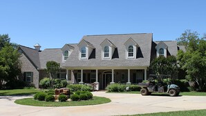A large, two-story house with a symmetrical facade, a covered front porch, and a driveway with a utility vehicle parked in front. - Whitetail Ranch Manor Retreat (Bryan)