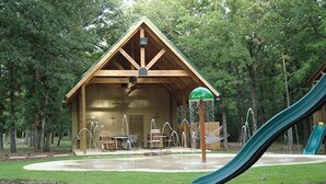 A wooden cabin with a covered patio, a water feature, and a green slide. - Whitetail Ranch Manor Retreat (Bryan)