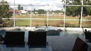 Un espace piscine équipé d’une table et de chaises, d’un jacuzzi et offrant une vue sur un terrain de golf grâce à de grandes fenêtres.