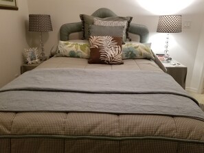 Ein ordentlich bezogenes Bett mit einer karierten Tagesdecke und mehreren Kissen, darunter eines mit Zeprazieher.