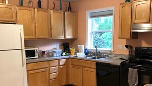 A kitchen with wooden cabinets, a white refrigerator, a microwave, a stove, and a window with a view of greenery outside. - Narraganett 4BR, Pier Neighborhood, Walk 2 Amenities, Dog-friendly, dead-end st. (Narragansett)