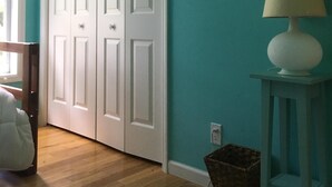 A room with teal walls, a white door, a round mirror, a white lamp on a small table, and a wooden floor. - Narraganett 4BR, Pier Neighborhood, Walk 2 Amenities, Dog-friendly, dead-end st. (Narragansett)