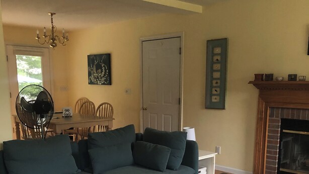 A living room with a sectional sofa, a glass-top coffee table with decorative items, a dining area with a table and chairs, a fireplace, and a door. - Narraganett 4BR, Pier Neighborhood, Walk 2 Amenities, Dog-friendly, dead-end st. (Narragansett)
