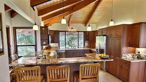 A kitchen with wooden cabinets, granite countertops, and a large island with bar stools. - Luxury Oceanfront Escape – A/C, Hot Tub, 5 bedrooms & Stunning Ocean Views! (Princeville)