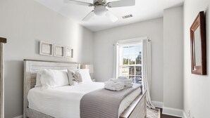 Une chambre à coucher avec un lit, un ventilateur de plafond, une fenêtre avec des stores et des tableaux encadrés accrochés au mur.