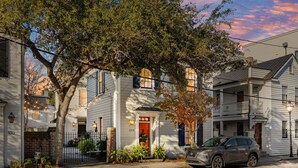 Une maison blanche à deux étages avec une porte rouge, un VUS garé devant et un arbre.