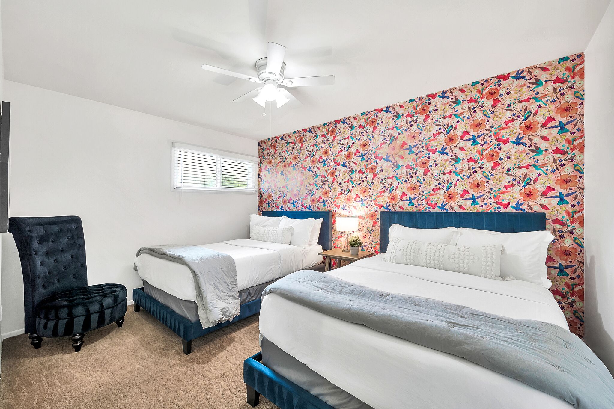 A bedroom with two single beds, a dark upholstered chair, a ceiling fan, and a floral-patterned headboard.