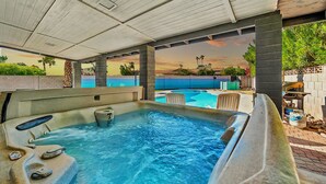 Un espace avec bain à remous offrant une vue sur la piscine, doté d’un plafond en bois et d’un coin salon extérieur.