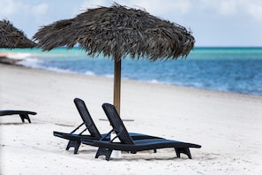 A beach scene with a straw umbrella and a lounge chair.