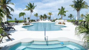 Un espace piscine agrémenté de chaises longues et de palmiers, entouré d’une terrasse blanche.