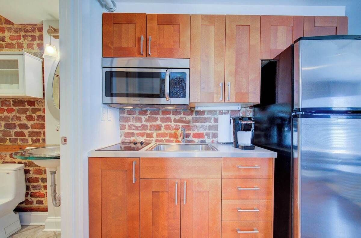 A compact kitchen with wooden cabinets, a stainless steel refrigerator, a microwave, and a sink.