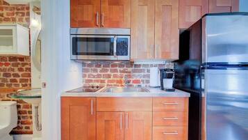 A compact kitchen with wooden cabinets, a stainless steel refrigerator, a microwave, and a sink.