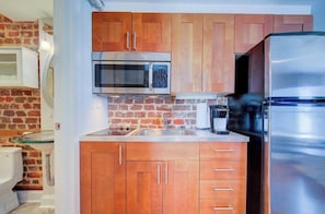 Cocina compacta con armarios de madera, refrigerador de acero inoxidable, microondas y un lavamanos.