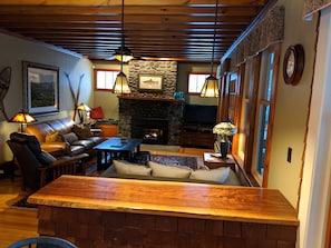 Un salon chaleureux avec une cheminée en pierre, un canapé en cuir, une table basse en bois et un coin bar.