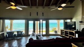 A living room with a large window overlooking the sea, a red sofa, two ceiling fans, and a television.