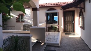A courtyard with a tiled floor, a small garden area with plants, a bench, and a door with a metal gate.