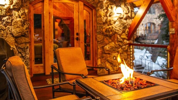 A stone-walled room with a wooden door, a fire pit with burning wood, and a view of the outside. - Refined creekside retreat • Barrel sauna overlooking the river • Hot tub • Starlight evenings • Minutes to Sundance (Sundance)