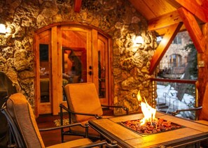Una habitación con paredes de piedra, una puerta de madera, un hogar con leña ardiendo y vistas al exterior.