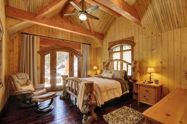 Dormitorio de cabaña de madera con una cama, una silla, una mesita de noche y un ventilador de techo.