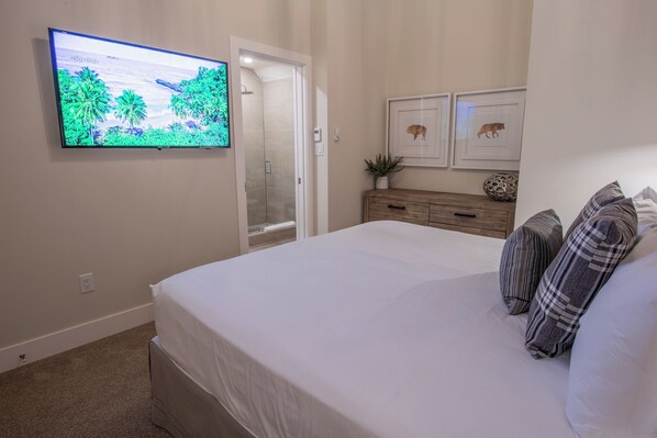 A bedroom with a large bed, a TV mounted on the wall, a wooden dresser, and a door leading to a bathroom. - Pinnacle Ridge 23 - Ski in Ski out, Private Hot Tub, Gas Fireplace (Whistler)