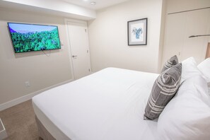 Un dormitorio con cama, televisor montado en la pared, un cuadro enmarcado y un armario.