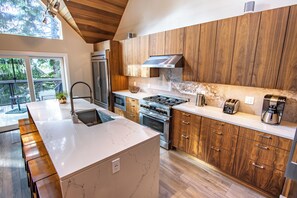 Een moderne keuken met houten kastjes, een marmeren aanrechtblad, roestvrijstalen apparatuur en een groot eiland.