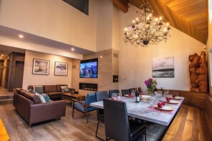 A modern living room with a fireplace, a dining area with a marble table, and a large chandelier. - Pinnacle Ridge 23 - Ski in Ski out, Private Hot Tub, Gas Fireplace (Whistler)