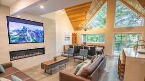 A modern living room with a fireplace, comfortable seating, a TV, and large windows. - Pinnacle Ridge 23 - Ski in Ski out, Private Hot Tub, Gas Fireplace (Whistler)