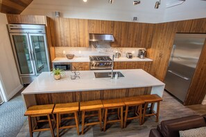 A modern kitchen with wooden cabinets, a large island with bar stools, stainless steel appliances, and a built-in oven. - Pinnacle Ridge 23 - Ski in Ski out, Private Hot Tub, Gas Fireplace (Whistler)