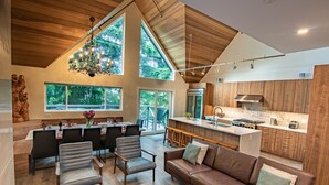 A spacious living area with a high ceiling, wooden beams, a dining table set for six, and a kitchen with wooden cabinets and stainless steel appliances. - Pinnacle Ridge 23 - Ski in Ski out, Private Hot Tub, Gas Fireplace (Whistler)