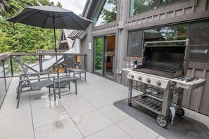 Un patio al aire libre con una estación de parrilla, una mesa con sillas y una sombrilla.