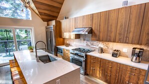 A modern kitchen with wooden cabinets, a marble countertop, stainless steel appliances, and a large island. - Pinnacle Ridge 23 - Ski in Ski out, Private Hot Tub, Gas Fireplace (Whistler)