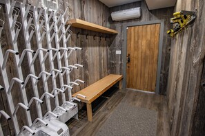 Un vestuario con varios taquillones blancos, un banco de madera, una puerta de madera y un perchero amarillo fijado a la pared.