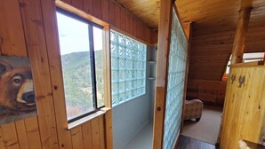 Interior de una cabaña de madera con una ventana, un banco de madera y un cuadro en la pared.