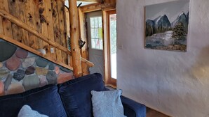 Interior acogedor de una cabaña con pared de piedra, escalera de madera y un cuadro de montañas.