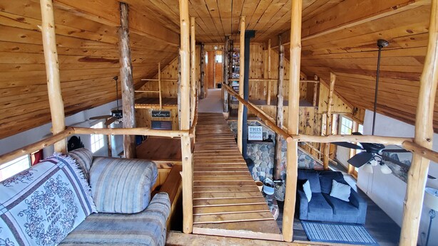 Un interior de madera con una escalera central de madera, un sofá y una pared de piedra.