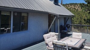 Una casa con techo metálico, un porche con muebles de exterior y vista a una ladera boscosa.