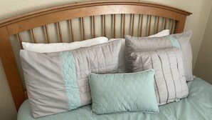 Una cama con cabecera de madera, varios cojines y una colcha verde claro.
