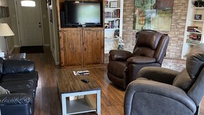 Una sala de estar con televisión, sofás de cuero, una mesa de centro y una estantería.