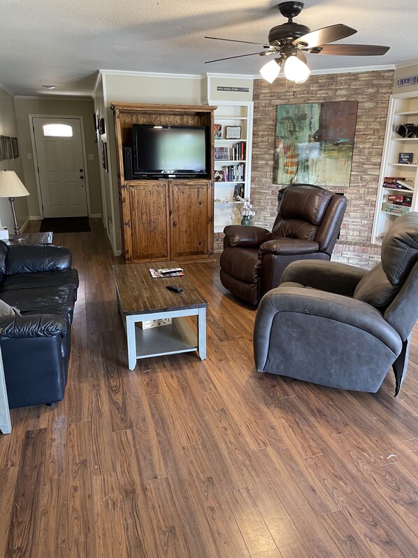 A living room with a television, leather sofas, a coffee table, and a bookshelf.
