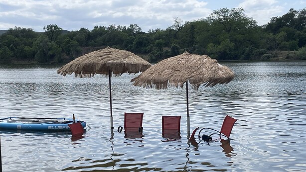 Un cuerpo de agua con dos sombrillas de paja y un bote inflable azul.