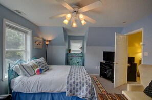 Ein Schlafzimmer mit einem Bett, einem Deckenventilator, einer Kommode, einem Fernseher und einer Tür zu einem anderen Raum.
