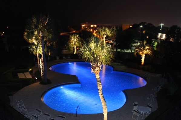 A nighttime view of a swimming pool with palm trees and lounge chairs.