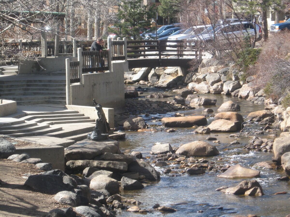 A stone bridge over a rocky stream with a parking area visible in the background.
