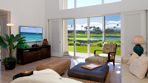 A spacious living room with a large TV, comfortable seating, and a view of a golf course through large sliding doors. -  Access to Mauna Lani Spa/Tennis/Pickleball/Gym/Lap Pool included with booking (Waimea)